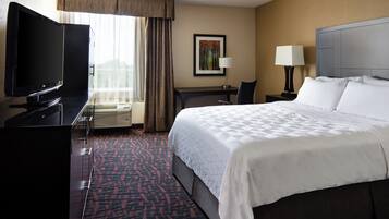 A hotel room with a large bed, a flat-screen TV, a desk with a chair, a window with curtains, and a painting on the wall.