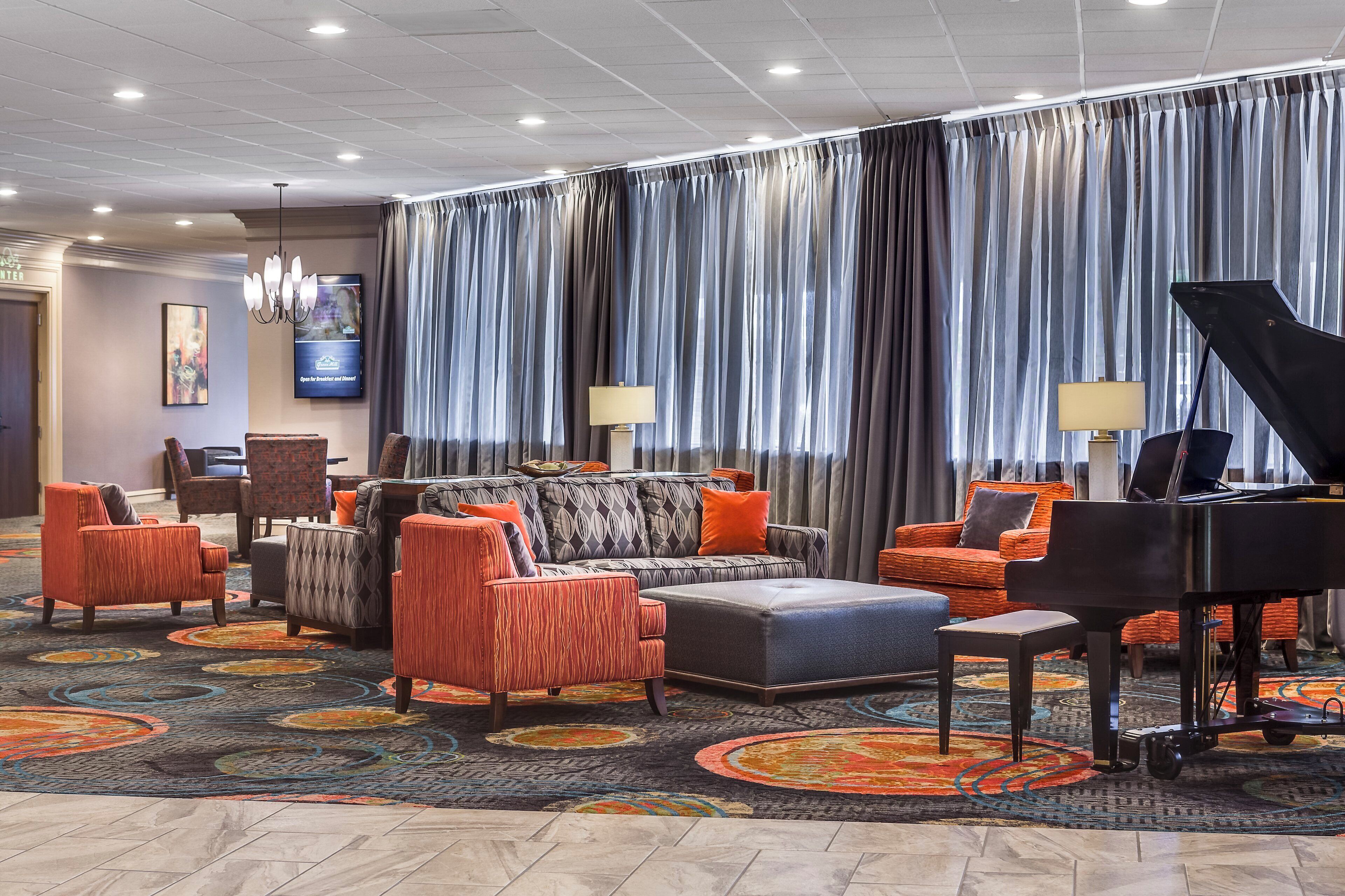 A hotel lobby with a seating area, a piano, and a television screen.