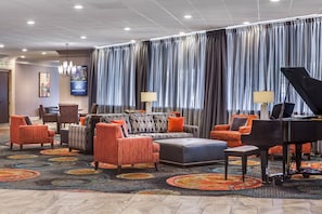 A hotel lobby with a seating area, a piano, and a television screen. - Holiday Inn Wichita East I-35 by IHG (Wichita)