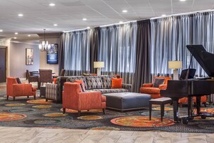 A hotel lobby with a seating area, a piano, and a television screen.