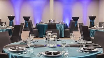 A banquet hall with round tables set for dining, each with a teal tablecloth, black chairs, and silverware.