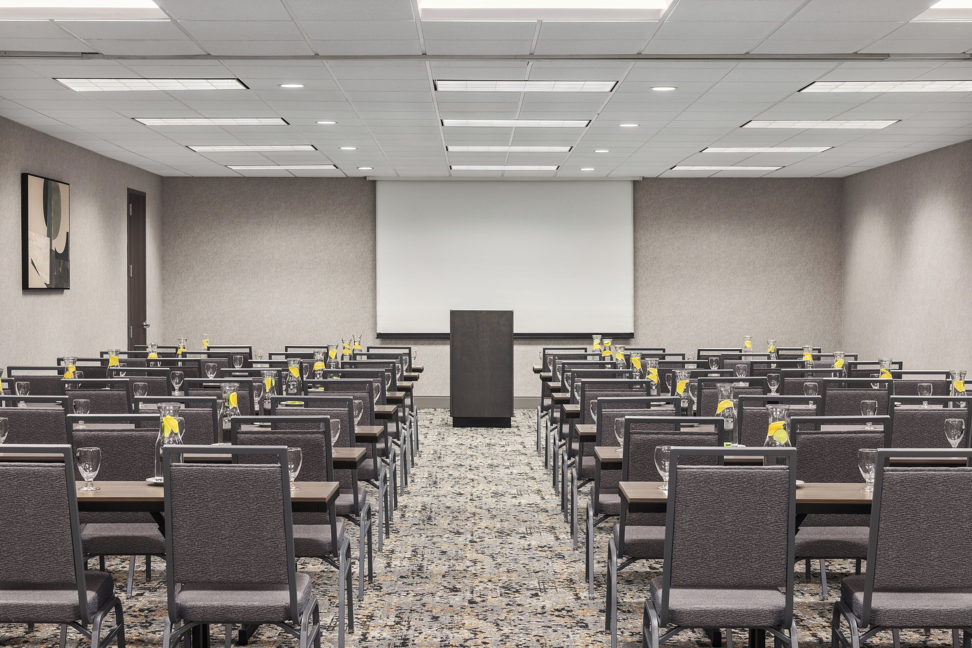 A conference room with rows of chairs, a projector screen, and a podium.
