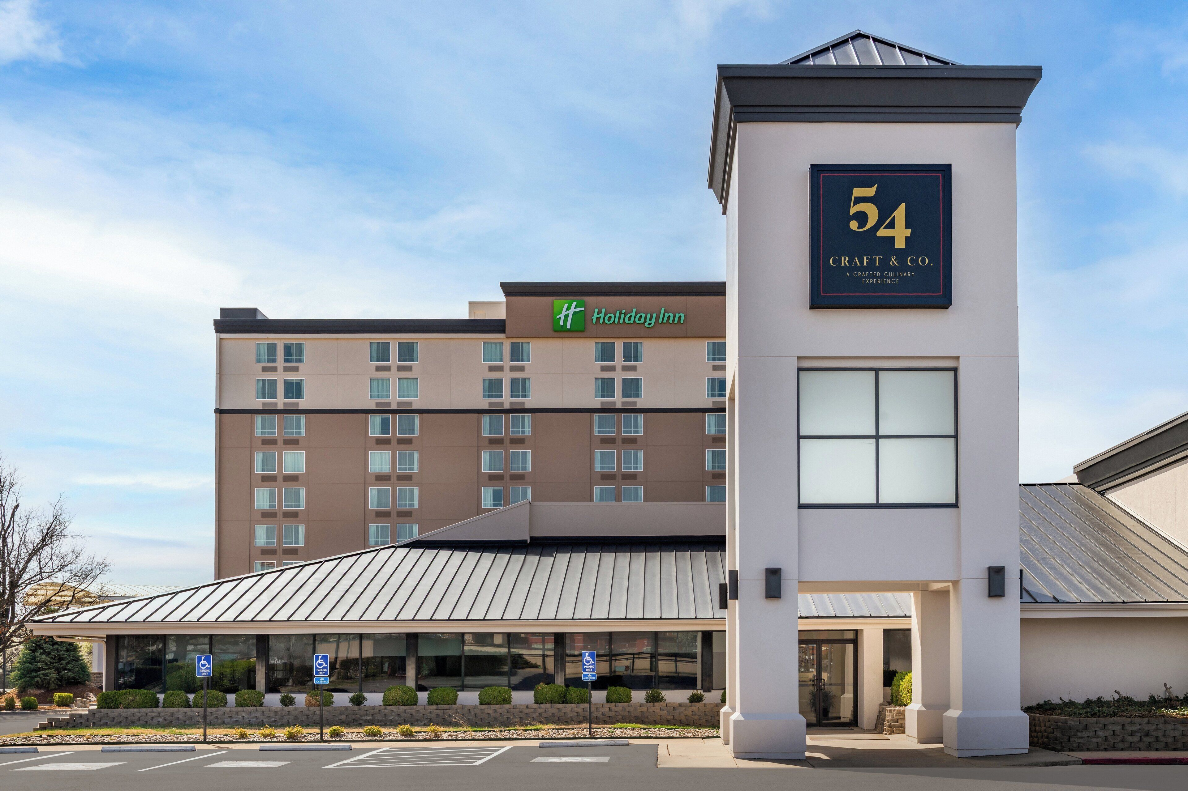A Holiday Inn hotel with a modern design, including a prominent number 54 sign, a covered entrance, and a parking area with handicapped accessibility signs.