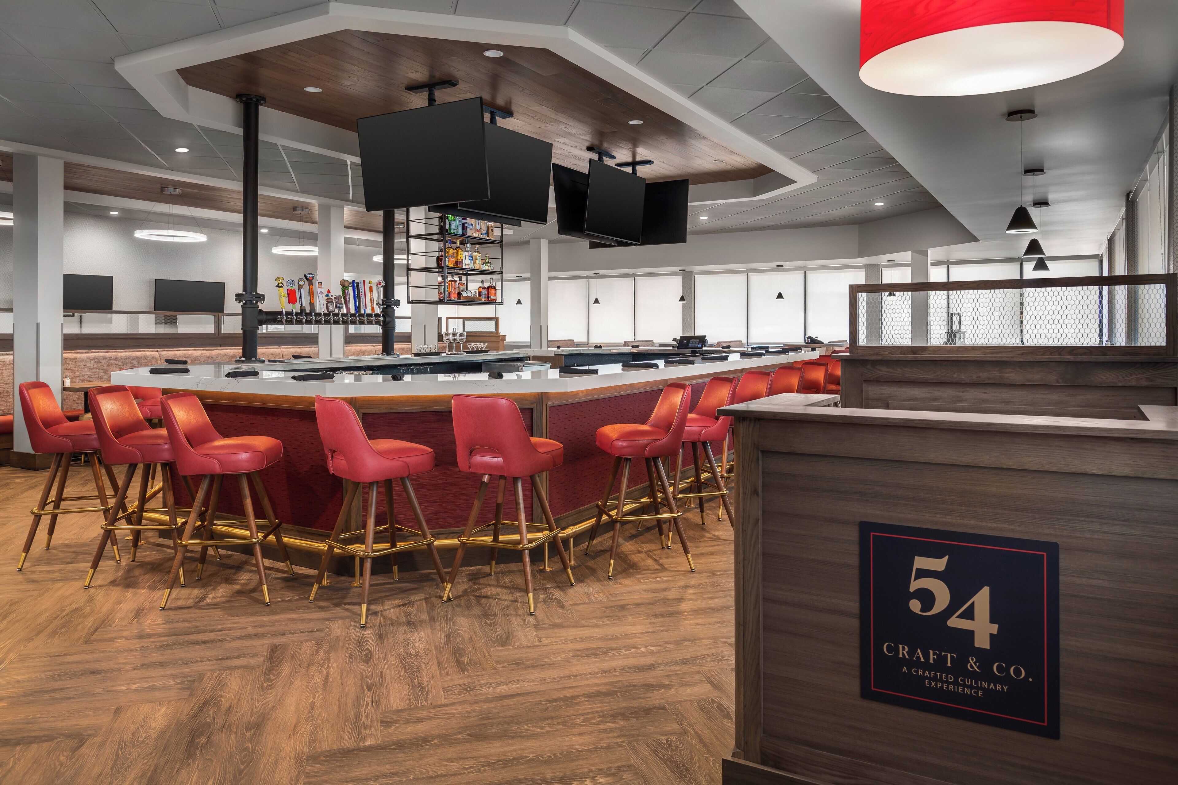 A modern bar area with a wooden counter, red bar stools, and a sign indicating the number 54 Craft & Co.
