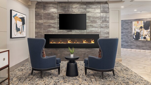 A modern lobby with a fireplace, two armchairs, a small table with a plant, and artwork on the walls. - Holiday Inn Wichita East I-35 by IHG (Wichita)