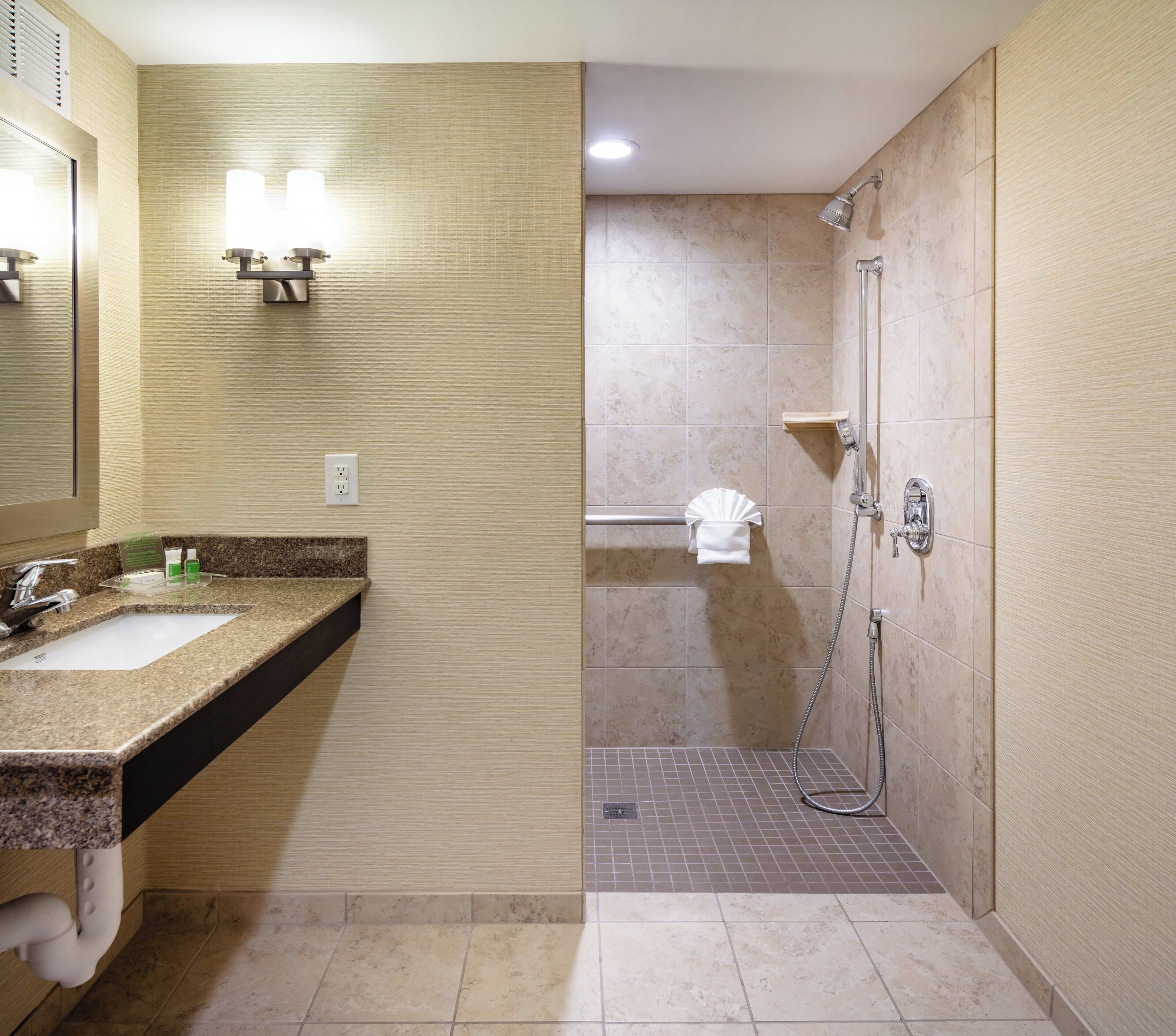 A modern bathroom with a granite countertop sink, a mirror, and a shower area with a handheld showerhead.