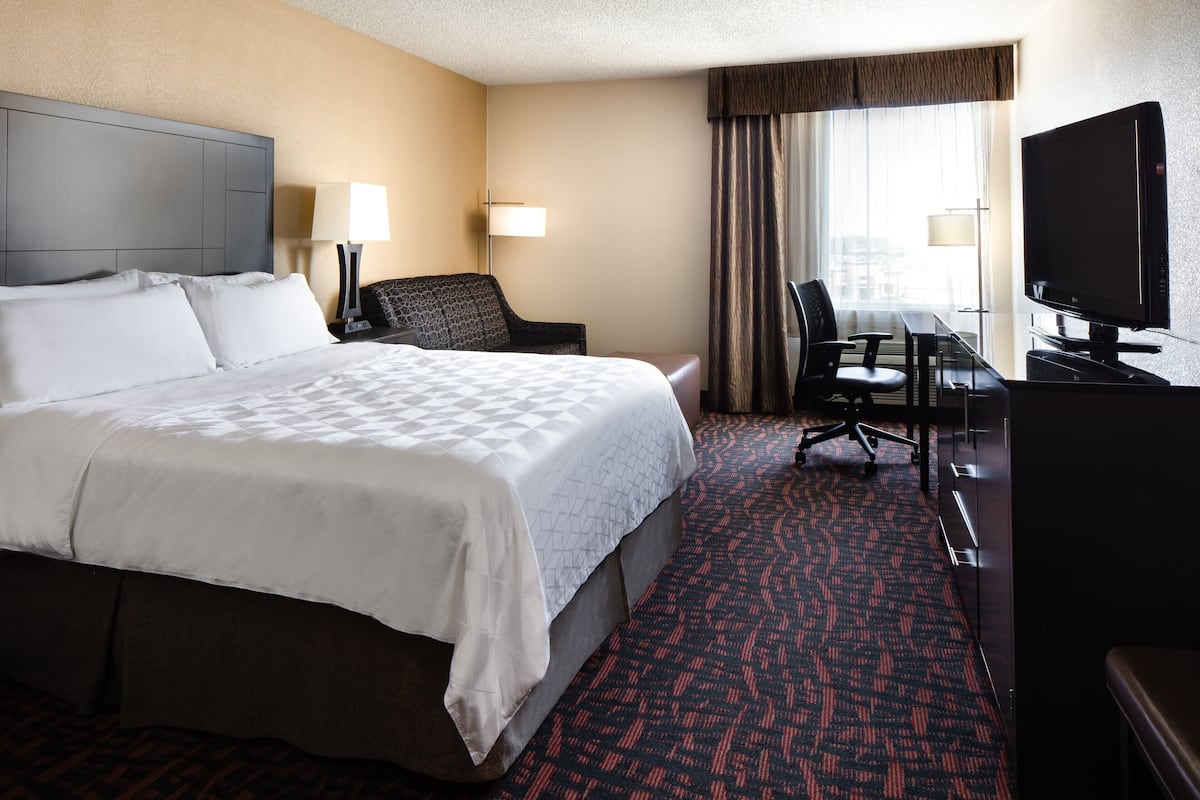 A hotel room with a large bed, a desk with a chair, a television, and a window with curtains.