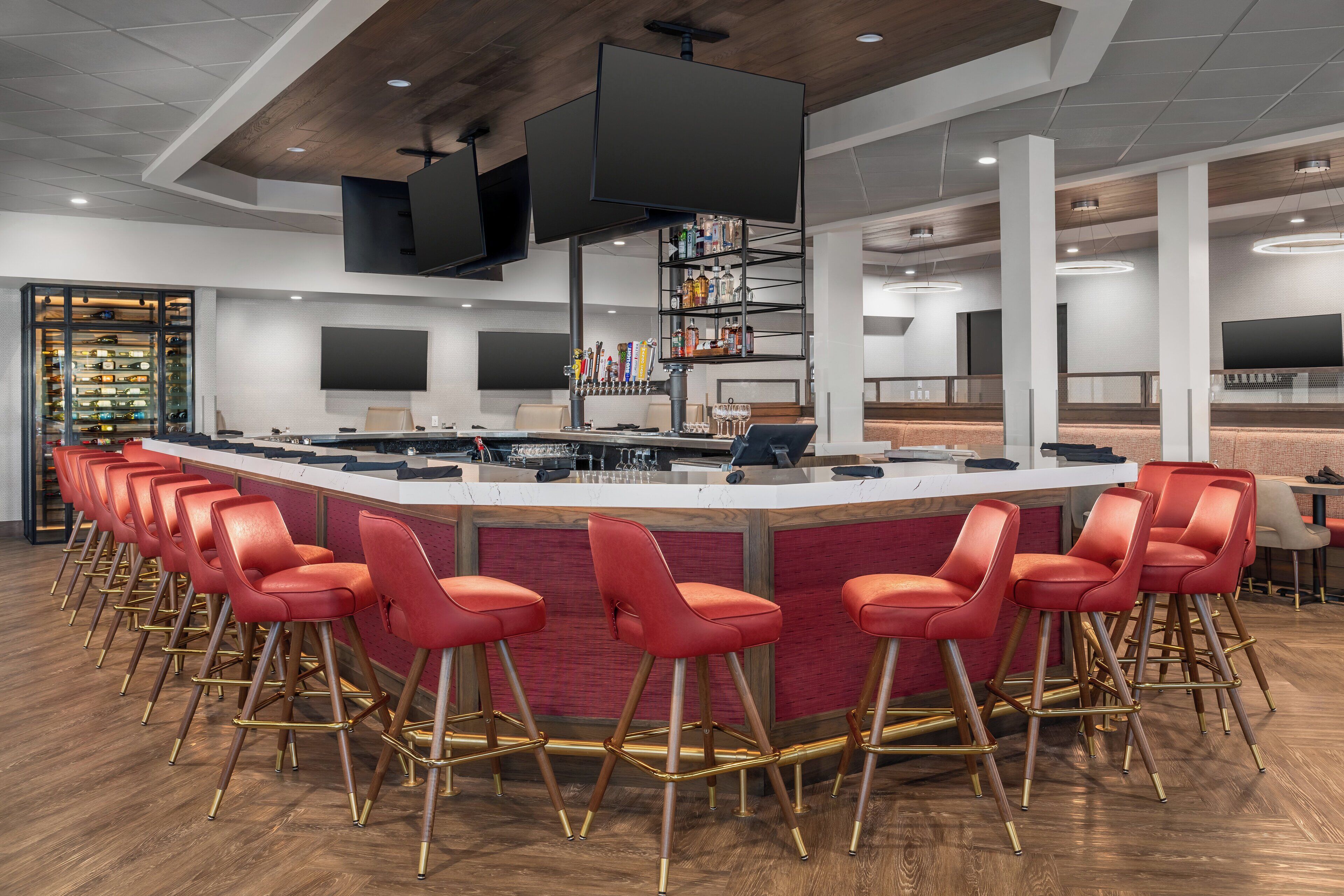 A modern bar area with a long counter, red bar stools, and a variety of bottles on shelves.