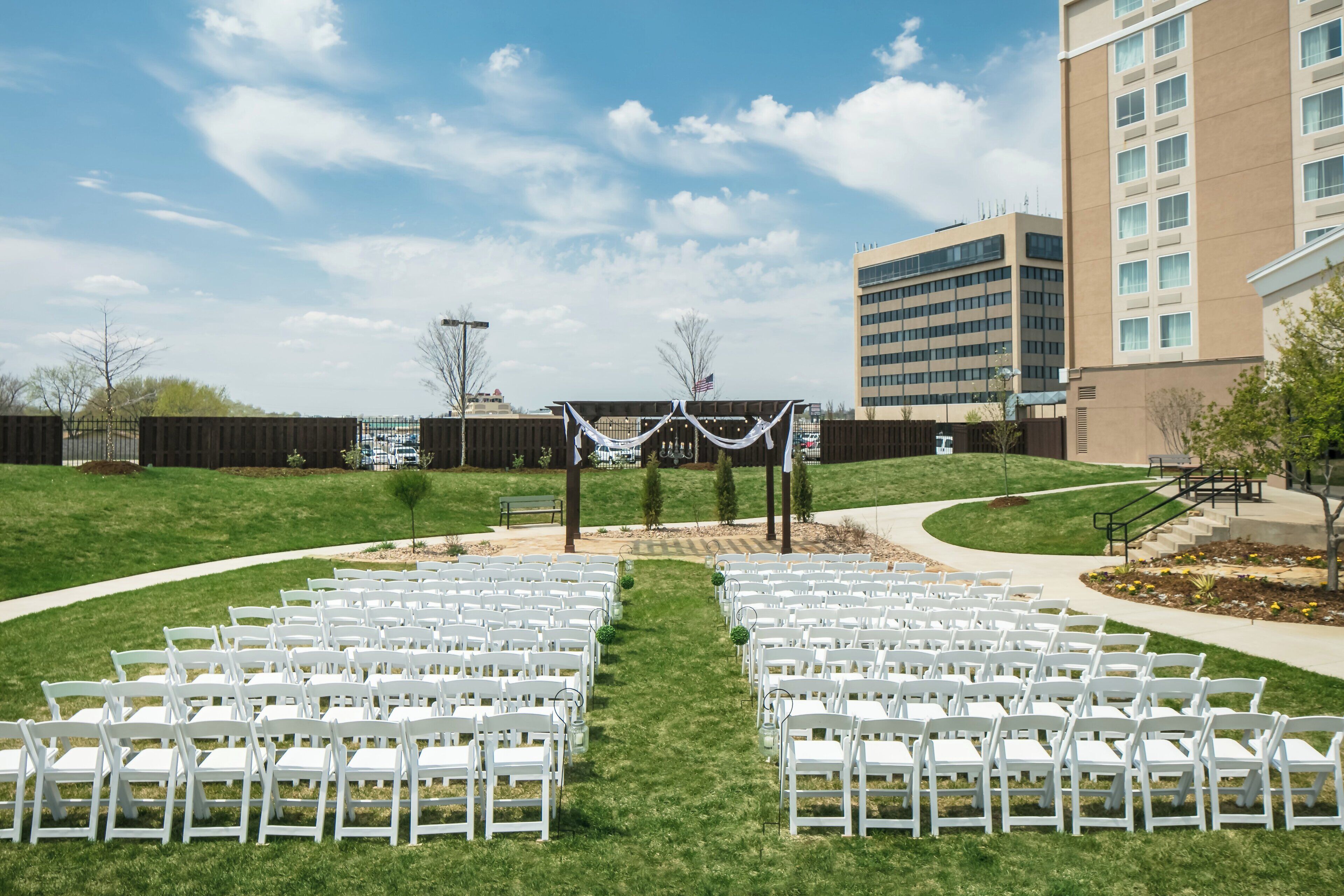 An outdoor seating area with white chairs arranged in rows, a covered walkway, and a building in the background.