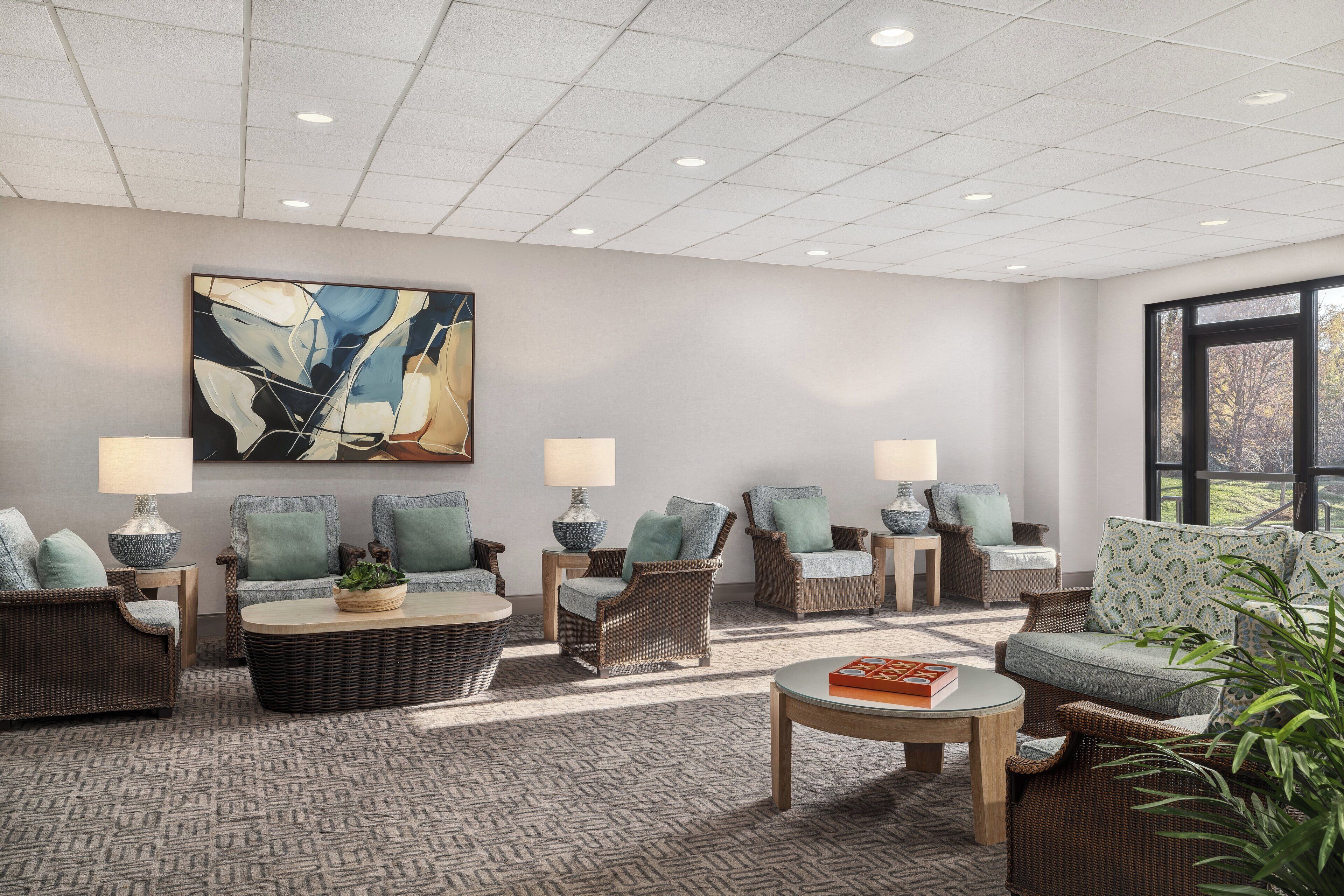 A modern lounge area with wicker furniture, a large abstract painting, and a view through a large window.