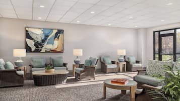 A modern lounge area with wicker furniture, a large abstract painting, and a view through a large window.