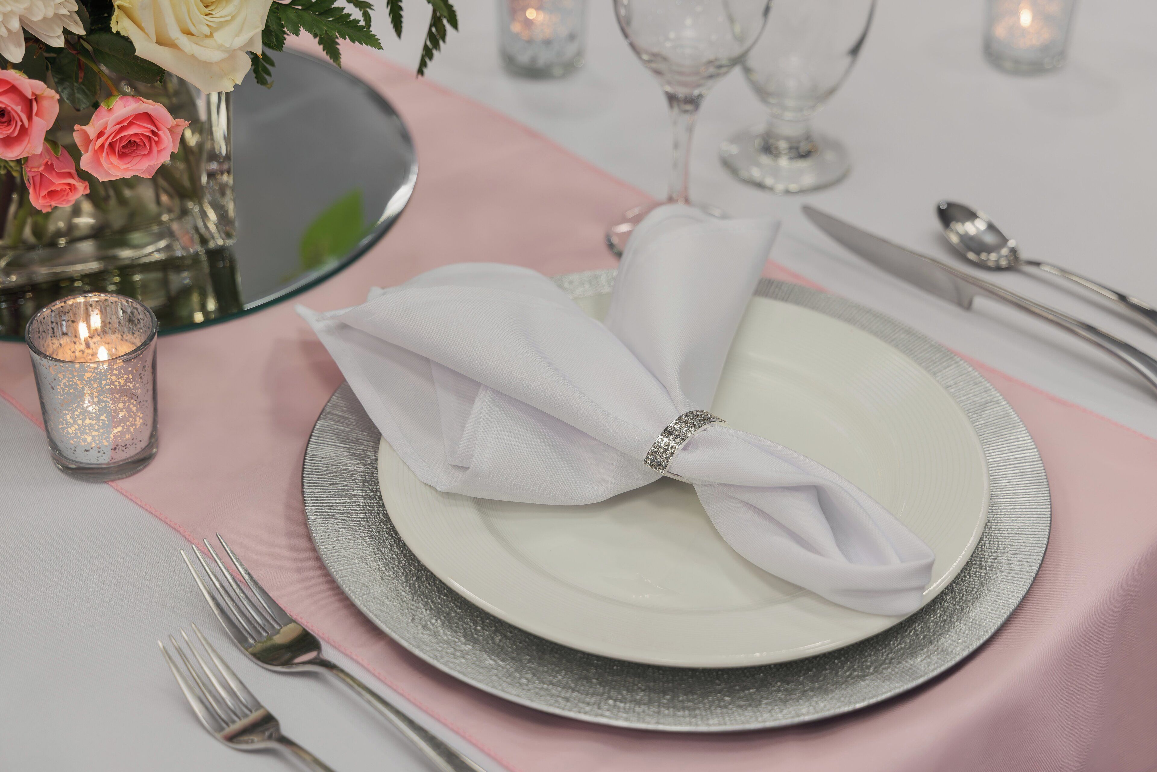 A table set with a white plate, silverware, and a pink napkin.