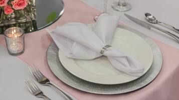 Una mesa con un plato blanco, cubiertos y una servilleta rosa.