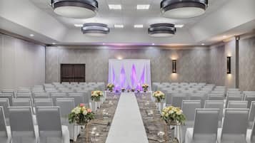 A conference room with rows of chairs, a white carpeted aisle, and floral centerpieces.