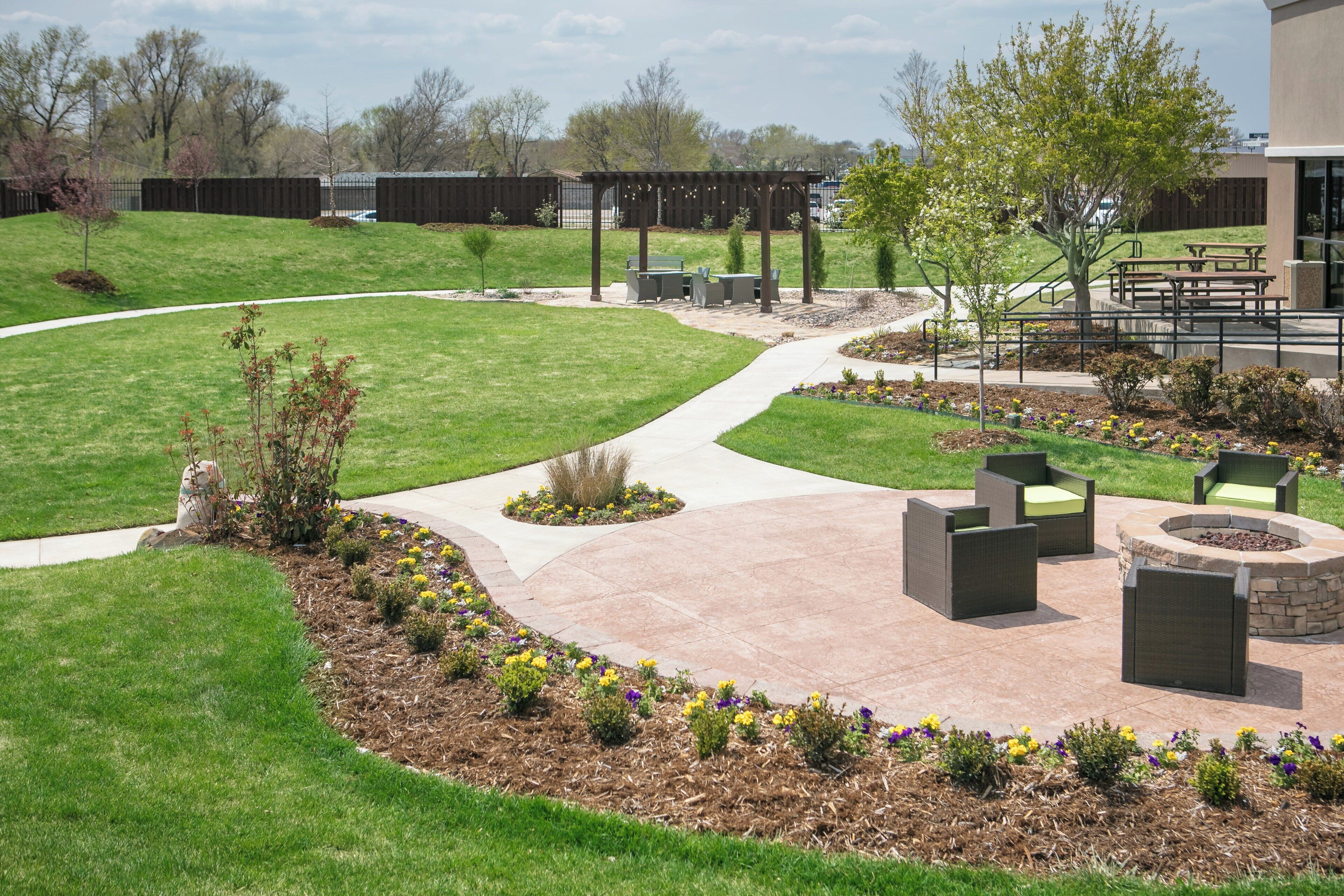A landscaped outdoor area with a curved pathway, seating arrangements, and a fire pit.