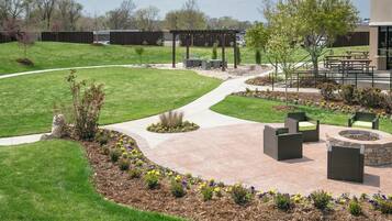 A landscaped outdoor area with a curved pathway, seating arrangements, and a fire pit.
