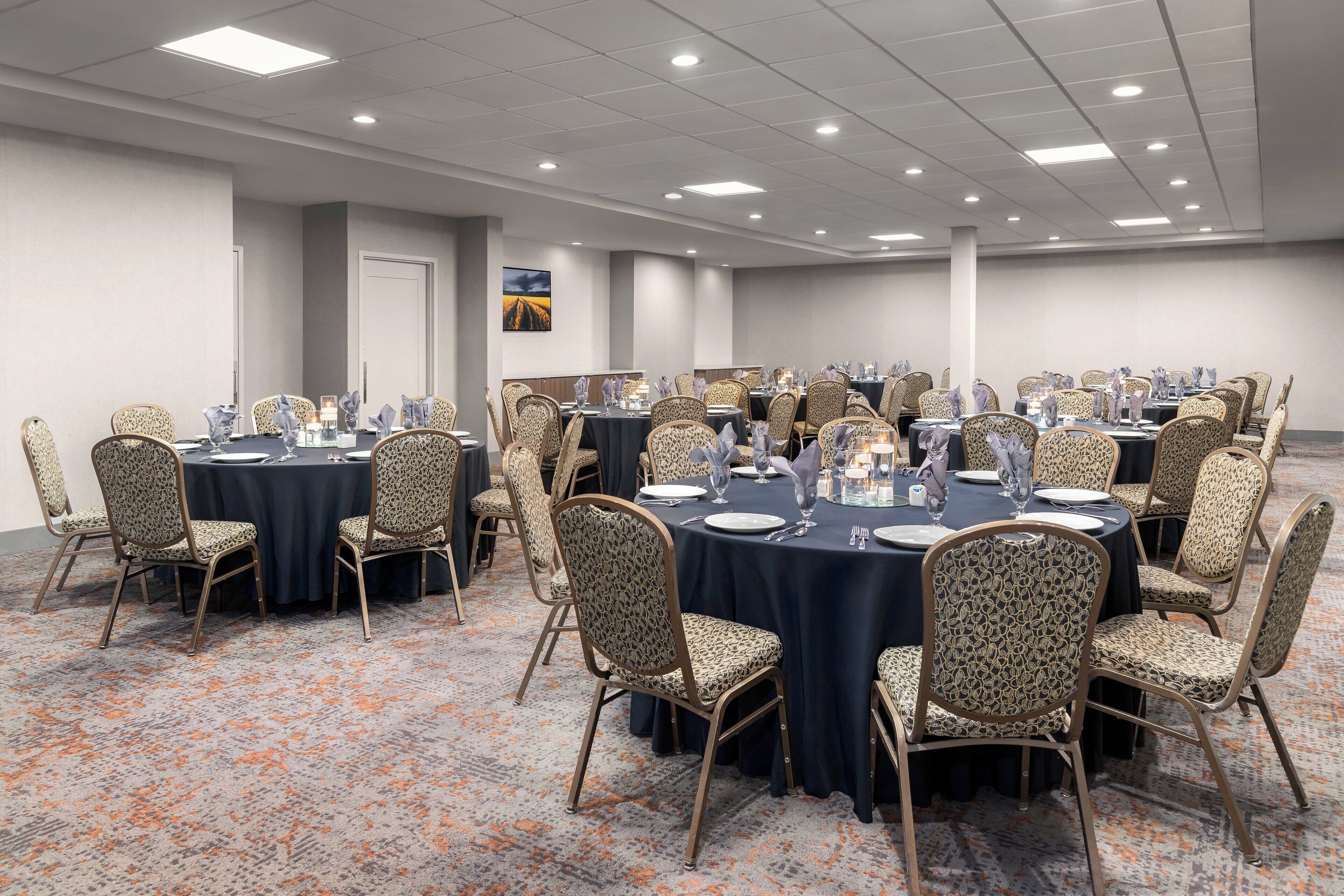 A conference room with round tables, patterned chairs, and a carpeted floor.