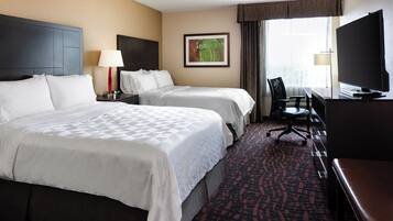 A hotel room with two beds, a desk, a chair, a television, and a window with curtains.
