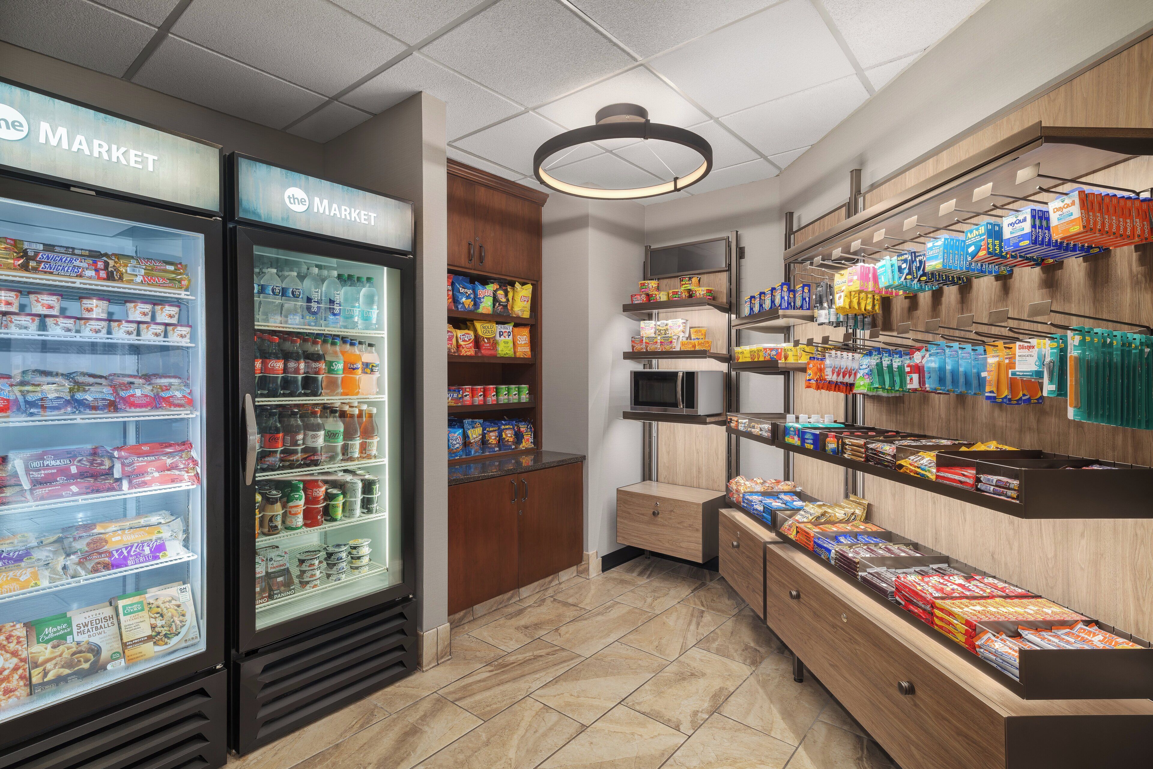 A grocery store interior with refrigerated sections, shelves stocked with snacks, and a microwave.