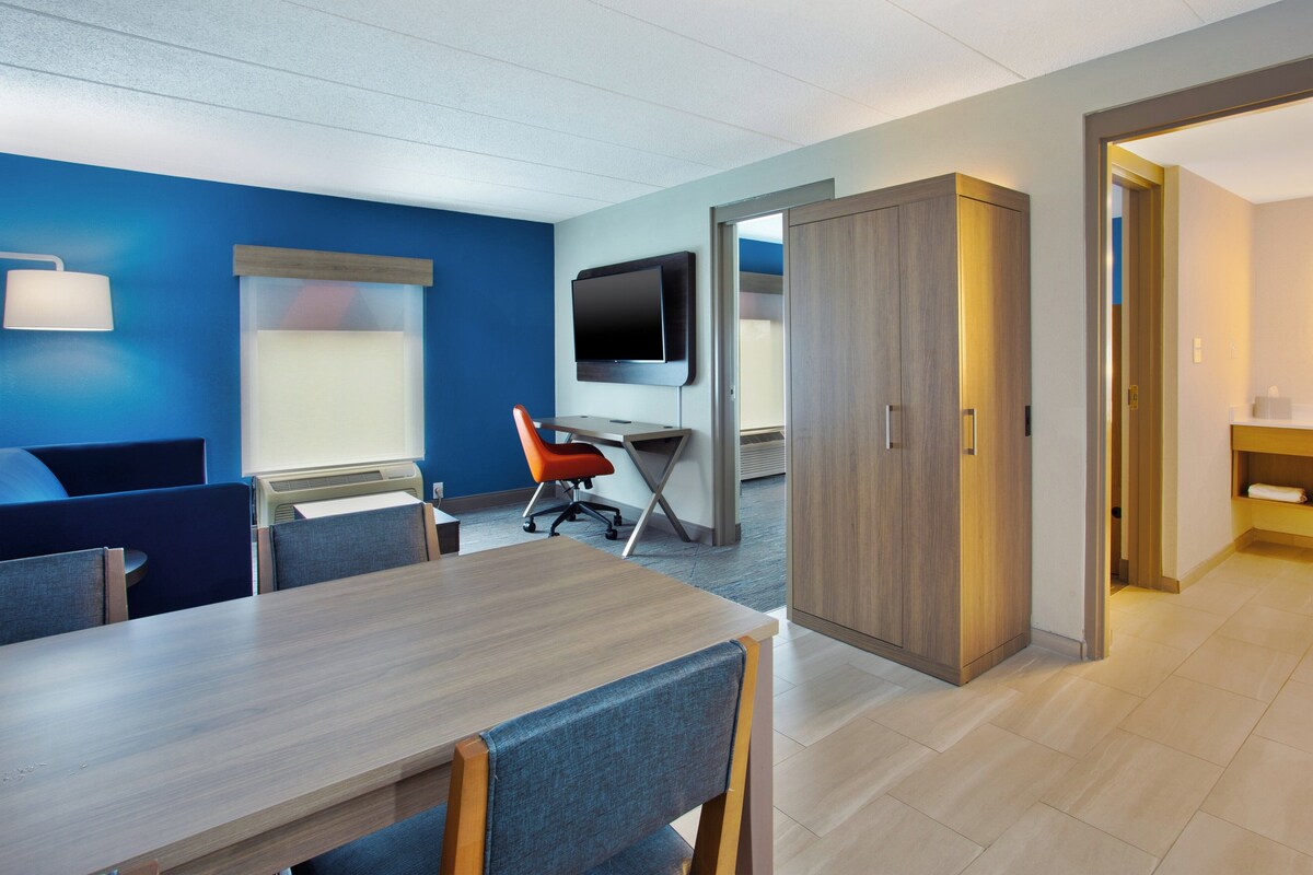 A modern hotel room with a wooden desk, blue walls, a television, and a wardrobe.