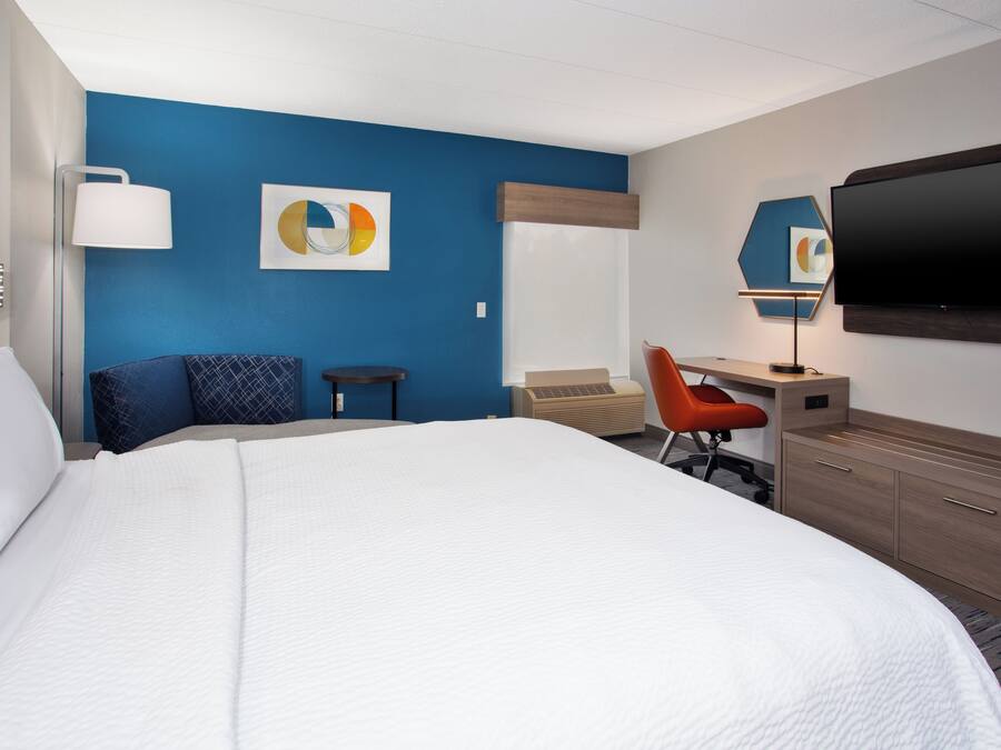 A hotel room with a large bed, a desk, a chair, a TV, and artwork on the walls.