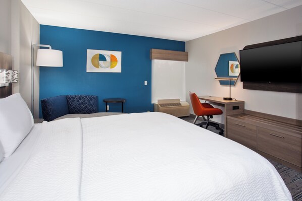 Una habitación de hotel con una cama grande, un escritorio, una silla, un televisor y obras de arte en las paredes.