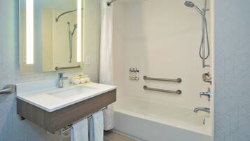 A modern bathroom with a bathtub, a shower, a vanity with a mirror, and handrails.