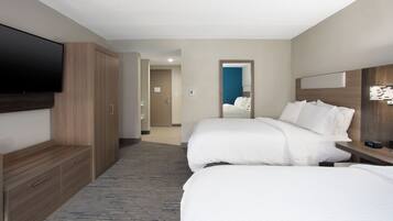 A hotel room with two beds, a flat-screen TV, wooden wardrobe, and a mirror.