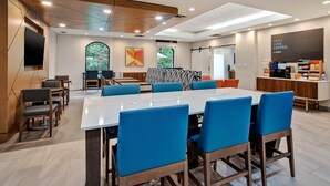A modern dining area with a long table, blue chairs, and a coffee station.