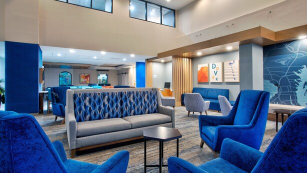 A modern lobby with a grey sofa, blue armchairs, and a small table. There are artwork on the walls and a map.