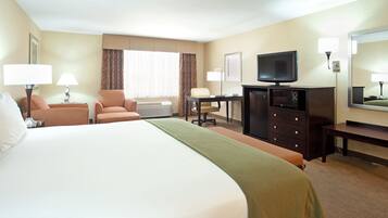Ein Hotelzimmer mit einem großen Bett, einem Schreibtisch, einem Sessel, einem Fernseher und einem Schminktisch.