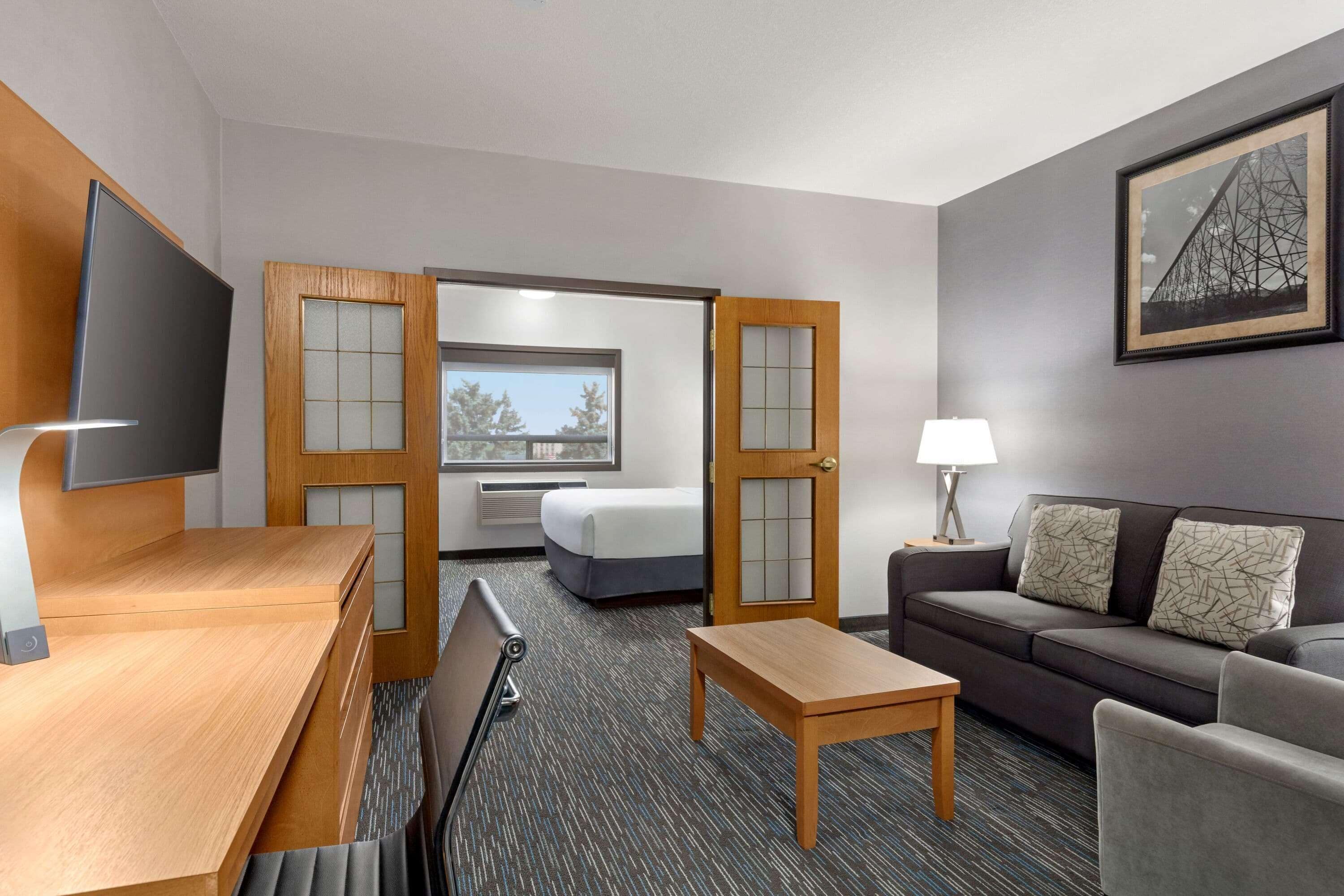 A hotel room with a wooden desk, a sofa, a bed, a TV, and a framed picture on the wall.