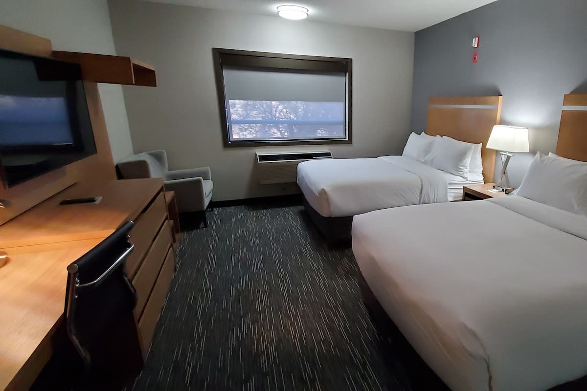 Hotellihuone, jossa on kaksi sänkyä, televisio, työpöytä tuolilla, ikkuna ja lamppu.