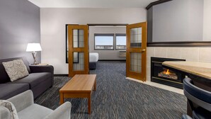 Habitación de hotel con sofá, mesa, chimenea y vista a la ciudad a través de amplias ventanas.