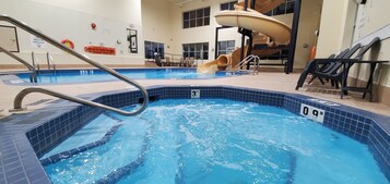 An indoor swimming pool with a slide, lounge chairs, and a diving sign.