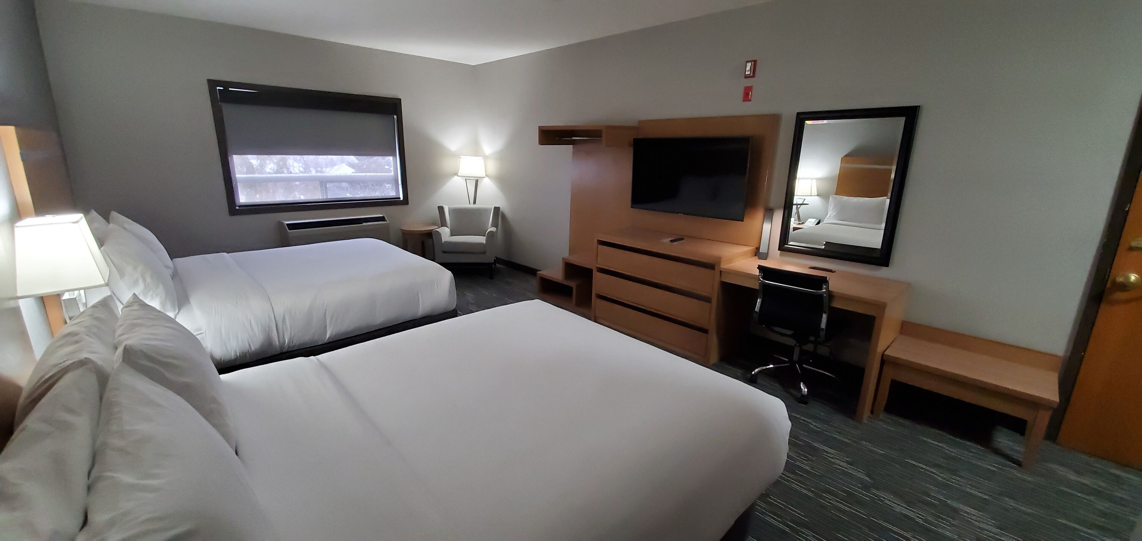 Una habitación de hotel con dos camas, un escritorio con una silla, un televisor y un espejo.