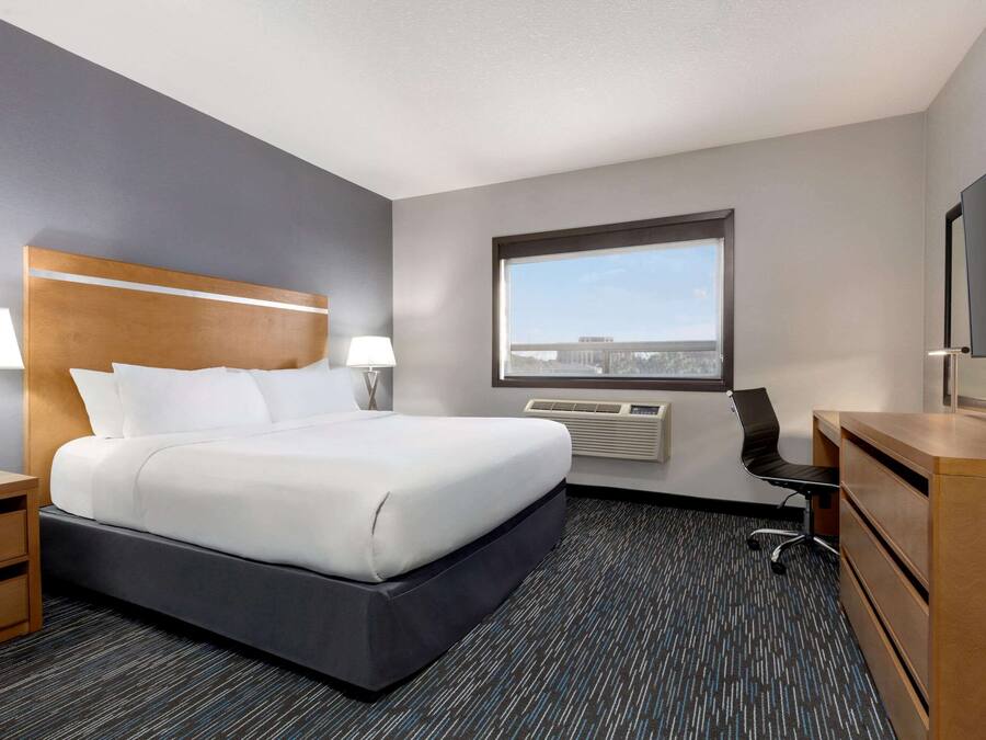 A hotel room with a large bed, a desk, a chair, a TV, and a window with a city view.