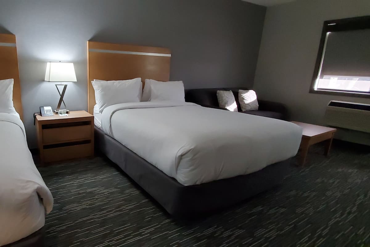 Hotellihuone, jossa on kaksi sänkyä, yöpöytä lampun kanssa ja pieni pöytä tuolilla.