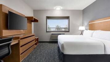 A hotel room with a bed, a flat-screen TV, a desk with drawers, a lamp, and a window with a view.