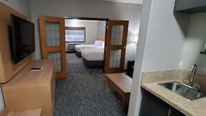 Una habitación de hotel con cama, televisión, escritorio y baño con lavabo.