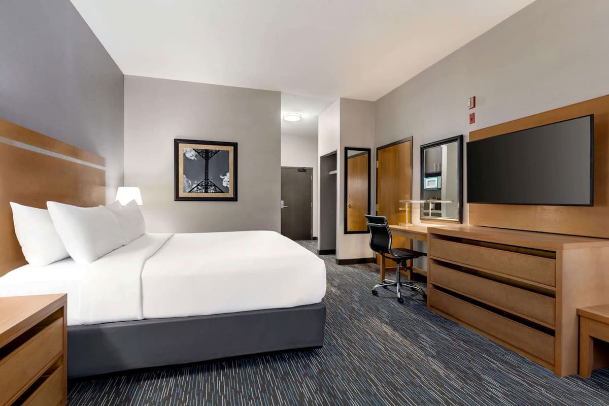 A hotel room with a bed, a desk, a chair, a mirror, and a picture on the wall.