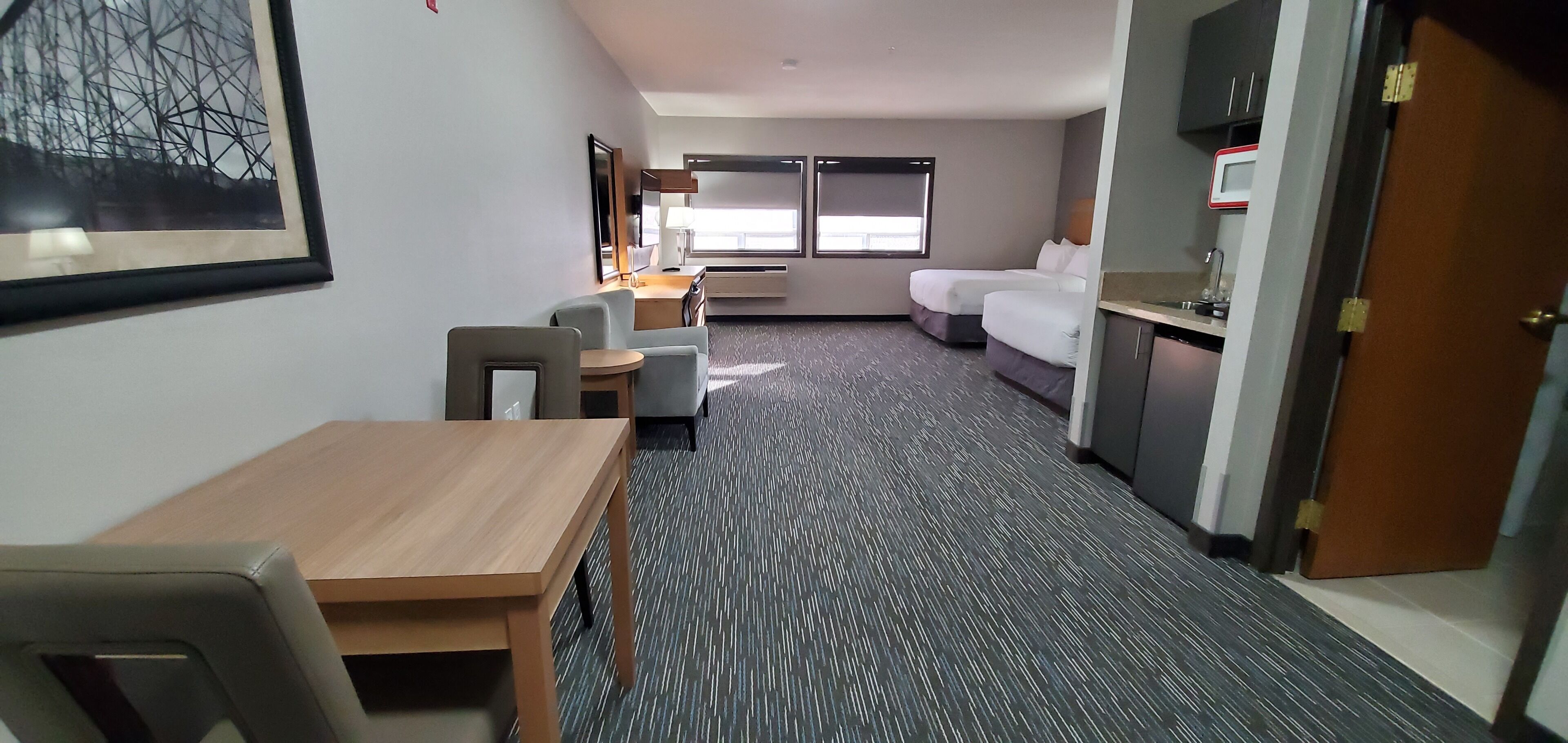Hotelkamer met een bed, bureau, stoel, een klein tafeltje, een bank, kitchenette en een raam met jaloezieën.