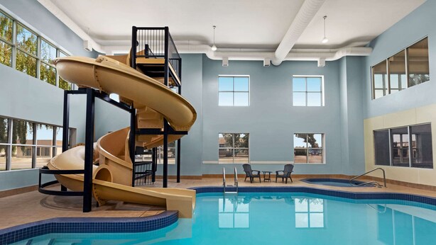 Una piscina interior con tobogán, zona de estar y amplios ventanales.