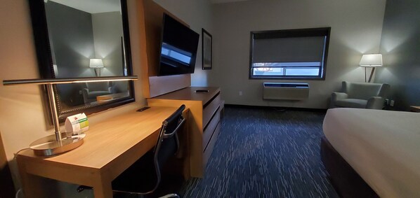 A hotel room with a bed, desk, chair, TV, window, and lamp.