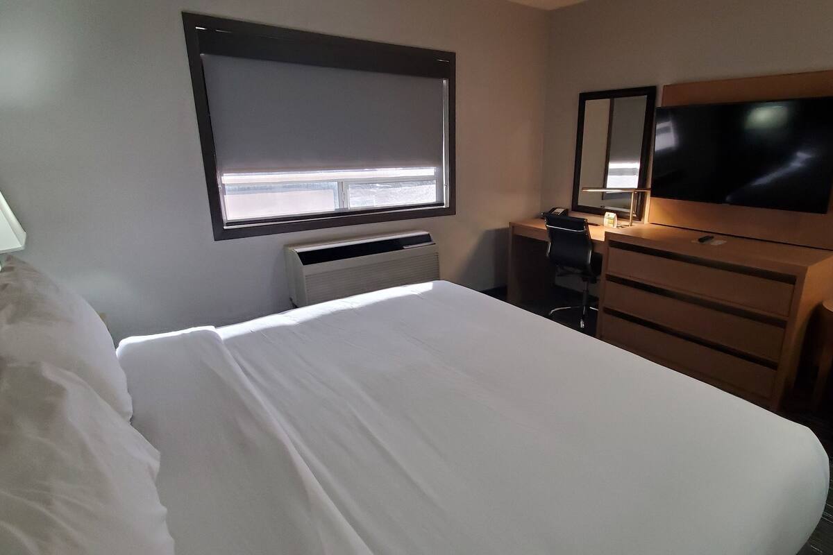 Hotellihuone, jossa on suuri sänky, työpöytä tuolilla, televisio ja ikkuna, jossa on sälekaihtimet.