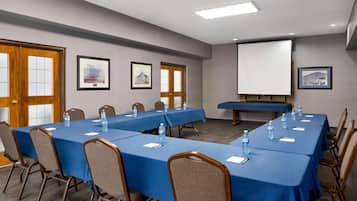 A conference room with long tables, chairs, and a projector screen.