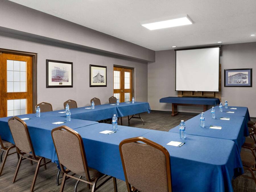 A conference room with long tables, chairs, and a projector screen.