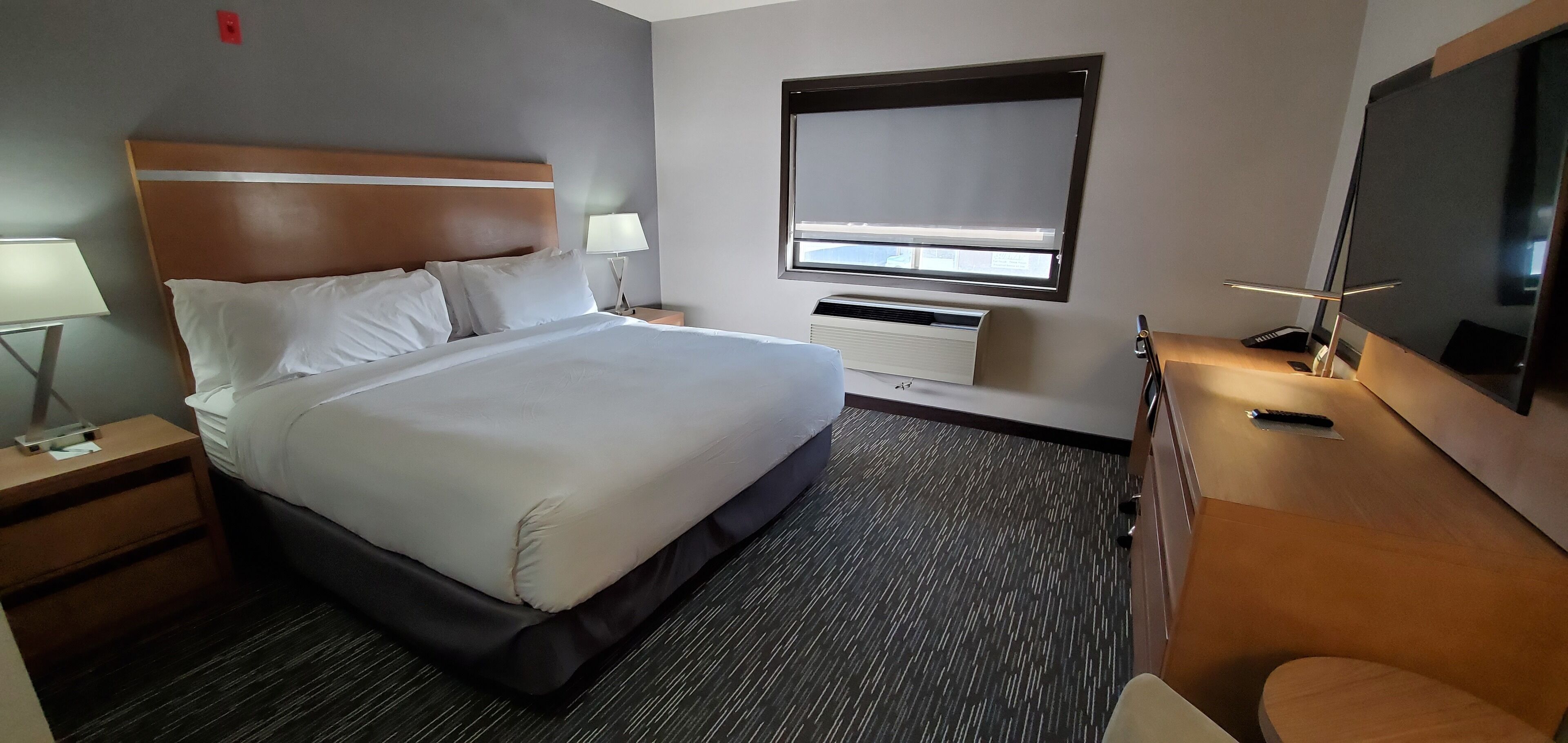 A hotel room with a large bed, a desk with a chair, a TV, and a window with blinds.