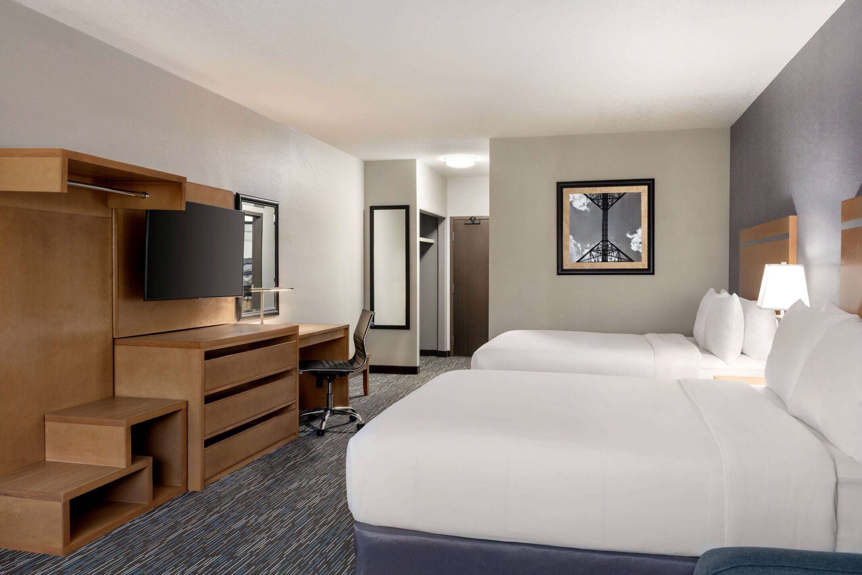 A hotel room with two beds, a desk with a chair, a TV, and a framed picture on the wall.