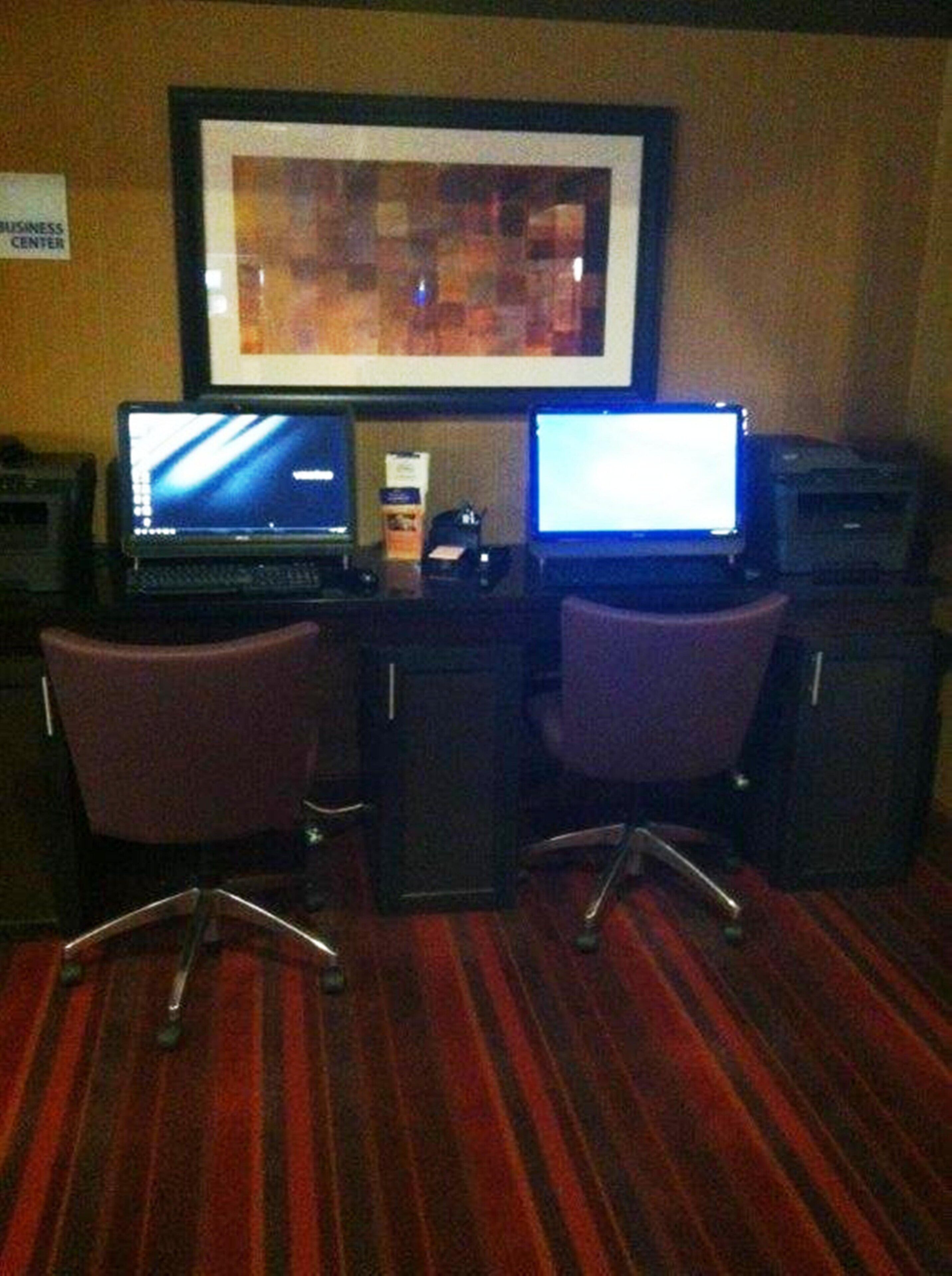 A business center with two laptops on desks, chairs, and a framed picture on the wall.